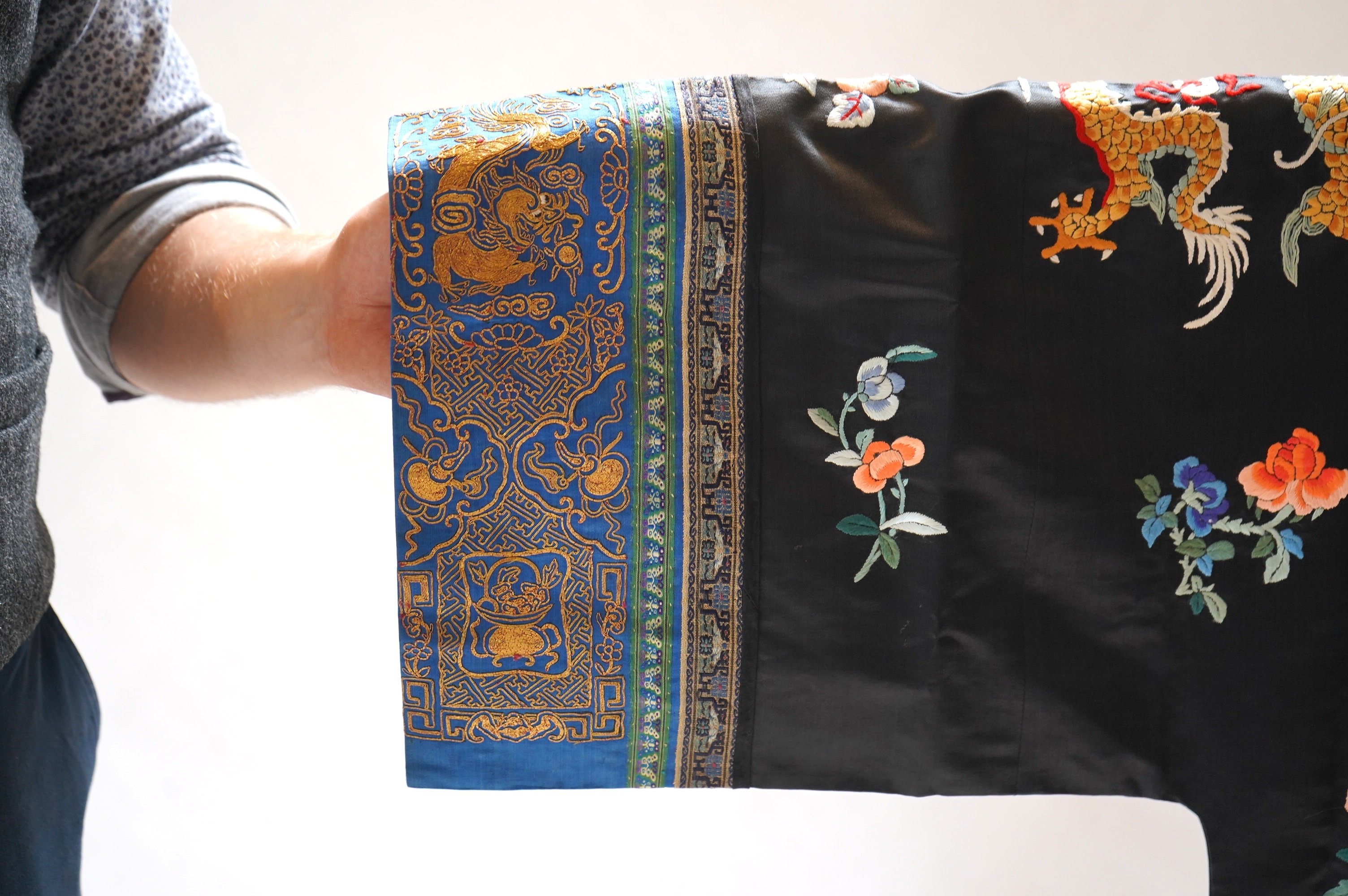 An early 20th century Chinese blue satin silk embroidered dragon robe, embroidered with five claw dragon symbols with flaming pearls, surrounded by bats and flower motifs, with gold thread embroidered dragon sleeve bands